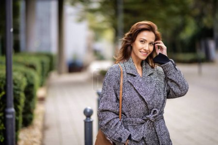 Téléchargez les photos : Portrait d'une femme moyenne adulte aux cheveux bruns marchant à l'extérieur dans la rue de la ville le jour de l'automne. Elle porte un manteau en tweed.. - en image libre de droit