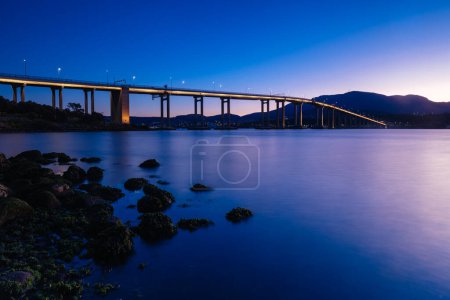 Téléchargez les photos : L'emblématique pont Tasman au crépuscule lors d'une soirée de printemps claire traversant le fleuve Derwent dans le centre de Hobart, en Tasmanie, en Australie. Tourné depuis l'estran de Clarence - en image libre de droit