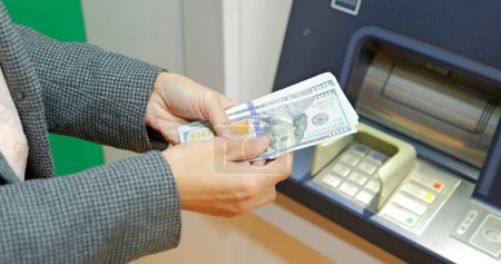 Téléchargez les photos : Femme mains avec USD dollar près de distributeur automatique de billets la nuit. Une fille qui retire de l'argent. Photo de haute qualité - en image libre de droit