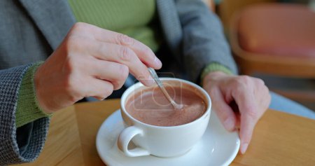 Photo for Girl hand stirs hot chocolate in white cup with spoon. Woman with creamy chocolate in cafe. High quality photo - Royalty Free Image
