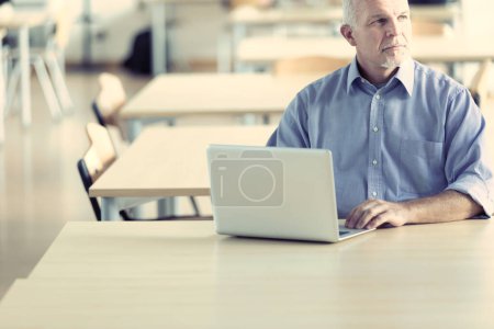 Hombre de edad avanzada utiliza un ordenador portátil en un ambiente de negocios brillante y moderno. Podría ser un investigador, un jubilado, un escritor. 
