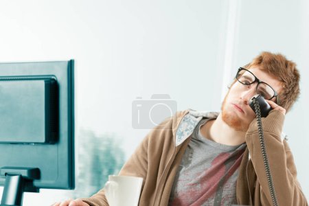 Funny image of young worker exasperated by ongoing telephone conversation. He is eyrolling and as a customer service representative waits patiently, but stresses himself a lot before consulting his customer