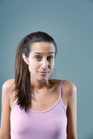 'What do I do now? I don't know.' Emotional portrait of young woman isolated on neutral background. Girl shows discomfort, doubt, every choice seems negative. Which is less worse? Long brown hair, sli