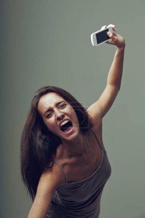 Wütendes Mädchen wirft wütend ihr Handy weg. Emotionales Porträt einer jungen Frau isoliert auf neutralem Hintergrund. Sie denkt: "Ich habe es satt, dass Smartphone und Internet nicht funktionieren!" während sie schreit 