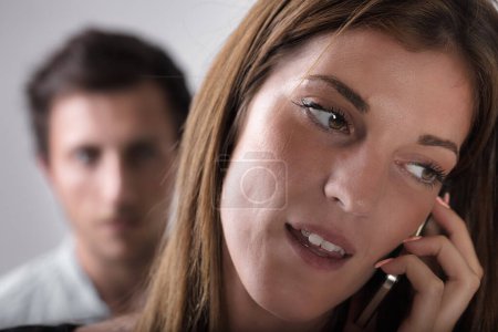 A woman on a phone call takes the foreground, with a blurred, suspicious young man in the backdrop. It insinuates betrayal, jealousy, love, stormy relations - the notion of a man's jealousy, frustrati