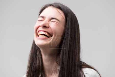 Porträt einer fröhlichen Frau, die lacht und lächelt. Sie trägt ein formales weißes Hemd, lange Haare, gute Zähne, strahlt Positivität und gute Nachrichten aus.