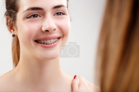 Primer plano de la chica sonriente mostrando frenos dentales a su dentista. Control profesional de ortodoncia y salud bucal, satisfactorio para el paciente