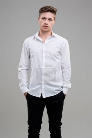 Klug gekleidet in einem weißen Hemd, vermischt sich sein Ausdruck mit lässiger Leichtigkeit und einem Hauch Entschlossenheit