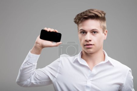 Tech-savvy jeune professionnel en chemise blanche tient smartphone, symbolisant la connectivité moderne et le style