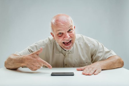 Exaggerated grimace and pointing fingers, man's demeanor around smartphone is teasingly dramatic