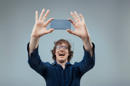 Man in blue shirt joyously holds up a transparent, high-tech phone, marveling at technology