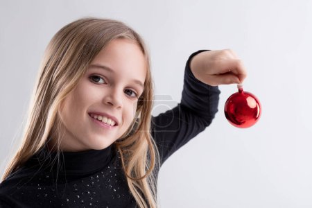 Freudiger Moment, als Mädchen mit strahlendem Lächeln eine leuchtend rote Weihnachtsdekoration zeigt