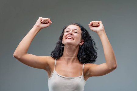 Mujer levanta sus brazos en un gesto triunfante, cabeza inclinada hacia atrás en una muestra de pura alegría.