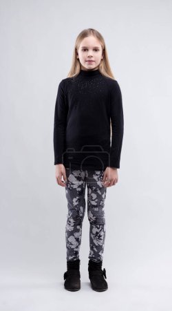 Girl in a black top and patterned leggings stands with a subtle confidence against a neutral backdrop