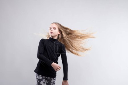 Child stands arms crossed, her hair caught in a burst of movement, reflecting youthful exuberance