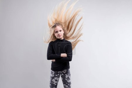 Young girl with dynamic hair motion, arms crossed, presents a mix of confidence and style