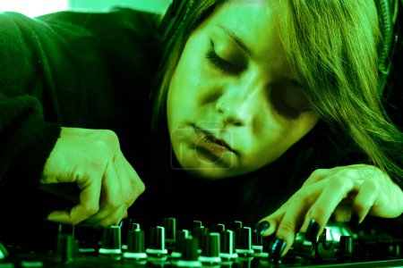 Deep in concentration, a woman DJs with precision under a haunting green light