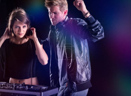 While the woman DJs with concentration, her partner exudes the energy of the music with a raised fist