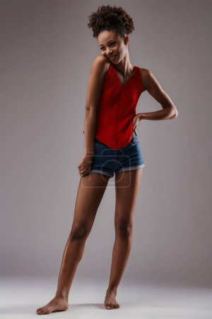 Standing barefoot, she personifies carefree elegance in a striking red top paired with classic shorts