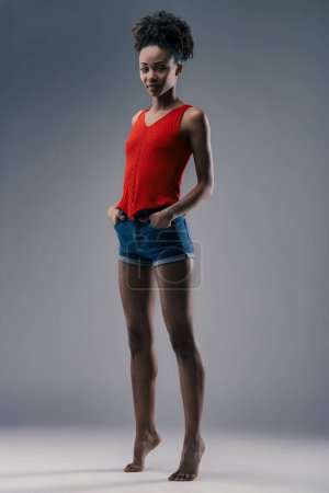 Frau in leuchtend rotem Tank-Top und Jeans-Shorts präsentiert einen entspannten, aber selbstbewussten Sommerstil