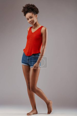 Elegancia casual personificada, mujer joven posa en pantalones cortos de mezclilla y vibrante top rojo