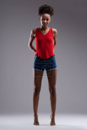 Con confianza de pie, la joven con una camiseta roja y pantalones cortos de mezclilla muestra una mezcla de fuerza y gracia