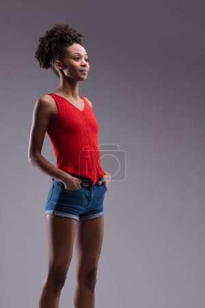 statuesque pose captures the woman's serene confidence, dressed in red and denim against a neutral background