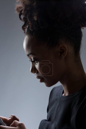Mujer joven inmersa en su smartphone, su rostro iluminado por la pantalla, mostrando una expresión reflexiva