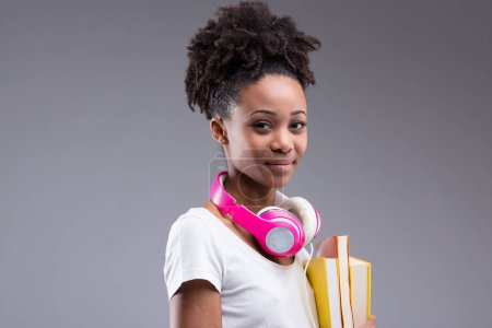 junge, buchkluge Frau lächelt selbstbewusst, rosa Kopfhörer um den Hals signalisieren Liebe zur Musik