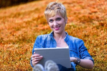 Short-haired woman explores her tablet, a fusion of technology and nature surrounds her