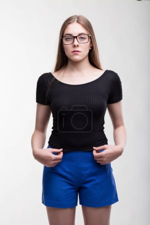 Determined woman in glasses stands confidently, contrasting black top with blue shorts