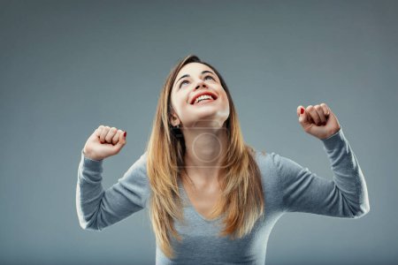 Femme jubilante dans un pull gris lève les poings dans un geste de victoire et de force