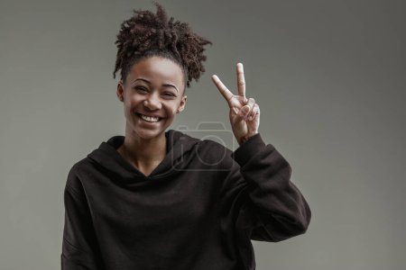 Gleeful expression on young woman's face as she displays a peace sign, dressed in casual hoodie