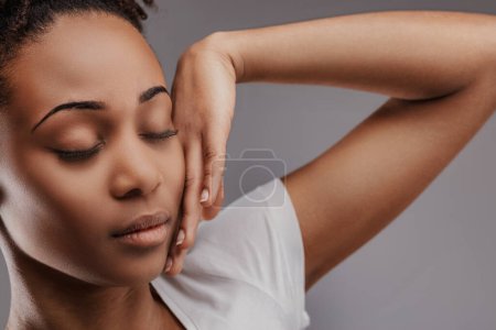Young black lady exudes tranquility with eyes closed, hand on cheek
