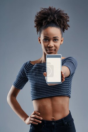 Young woman's vibrant smile brightens as she presents a smartphone, symbolizing connectivity and innovation