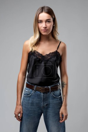 Modisch in dunklem Spaghettirock und Jeans gekleidet, wird der minimalistische Stil der Frau durch ein detailliertes Tattoo auf ihrem Arm betont.