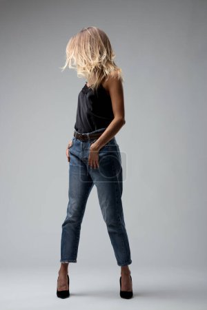 Looking off into the distance, she stands in jeans and heels, her pose relaxed yet full of dynamic tension