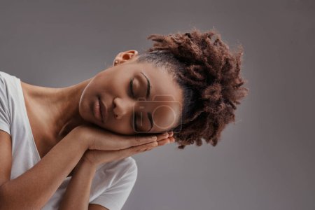 Jeune femme dans un sommeil paisible, mains croisées visage, incarne le calme sur un fond sourd