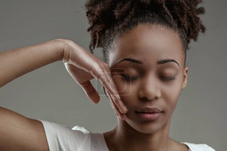 Gelassene junge schwarze Frau mit geschlossenen Augen, die Hand berührt sanft das Gesicht