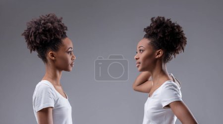 La duda de sí misma y el escrutinio interactúan en la postura de una joven mujer negra que evalúa su reflejo