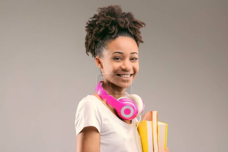 Estudiante ansioso con auriculares elegantes y un peinado afro, libros en la mano y sonrisa amplia