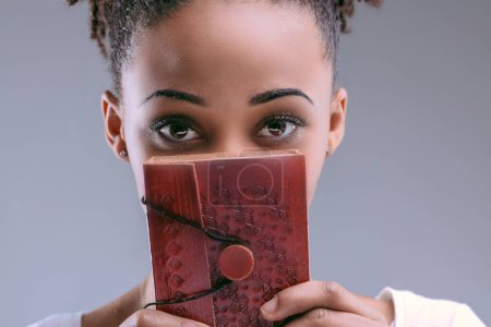 Young woman with enigmatic eyes peers over a richly embossed red journal, curiosity in her gaze