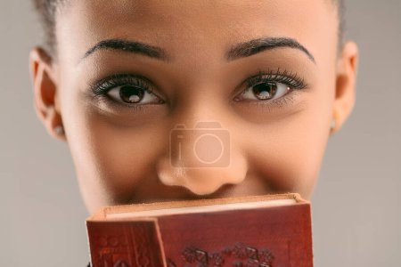 Young woman holding an ornate journal covers her face, leaving her intriguing eyes unveiled