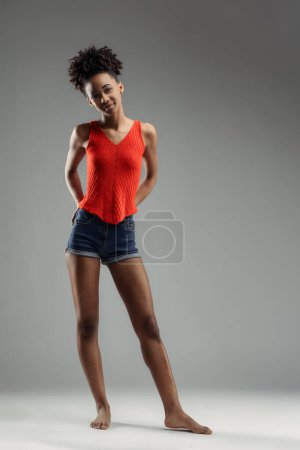 Young beautiful black woman in red tank top and denim shorts stands confidently