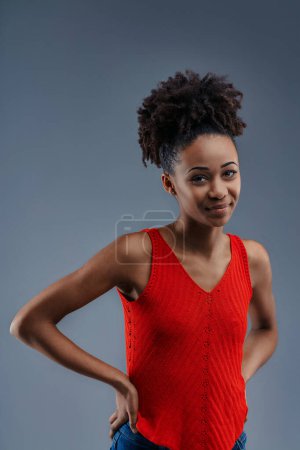 Casual and confident, a young woman with an afro stands hands on hips, smiling warmly
