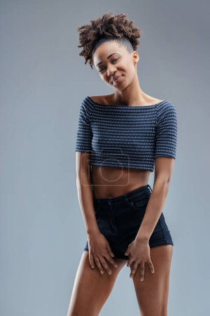 Young woman in a striped crop top and shorts shares a coy look, her posture relaxed and inviting