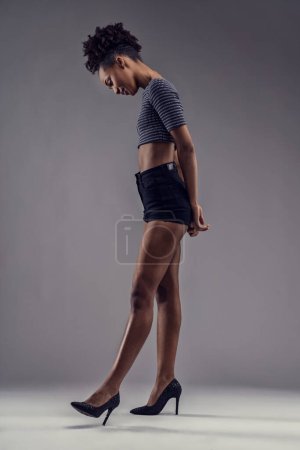 Postura con estilo de una joven hembra en pantalones cortos y tacones elegantes