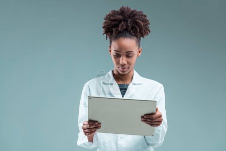 Jeune femme professionnelle examine attentivement une tablette, son regard intelligent absorbé dans le contenu de l'écran