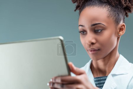 Mujer joven dedicada en una bata de laboratorio se sumerge en la investigación sobre su dispositivo portátil