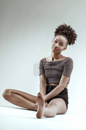Comfortable in her style, a young woman lounges with a soft expression